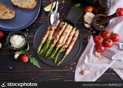 Healthy food - Asparagus wrapped with bacon and spices on a plate on wooden table.. Healthy food - Asparagus wrapped with bacon and spices on a plate on wooden table