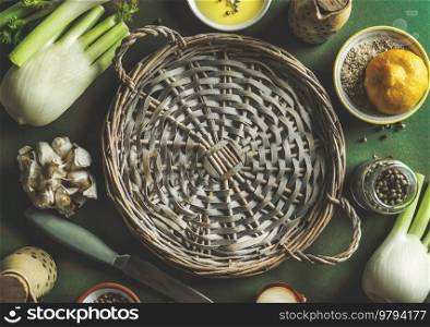 Healthy food background with empty wicker circle tray and cooking ingredients  fennel, lemon, oil and seasoning on green table, top view