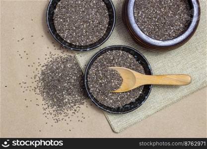 Healthy food, Chia seeds with spoon in black bowl on linen cloth and heap over cardboard background.