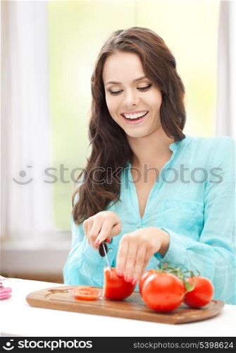 healthy food concept - beautiful woman in the kitchen cutting tomatoes