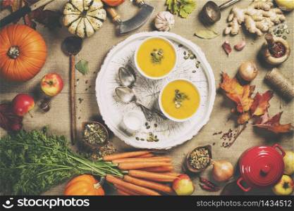 Healthy food cooking background. Vegetable ingredients and homemade soup. Fresh garden carrots, onions, pumpkins, ginger and spices on rustic wooden background, top view, copy space. Vegetable or pumpkin soup and ingredients flay lay top view