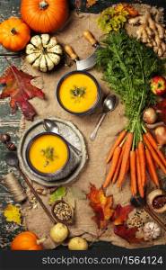 Healthy food cooking background. Vegetable ingredients and homemade soup. Fresh garden carrots, onions, pumpkins, ginger and spices on rustic wooden background, top view, copy space. Vegetable or pumpkin soup and ingredients, flat lay