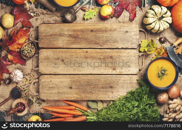 Healthy food cooking background. Vegetable ingredients and homemade soup. Fresh garden carrots, onions, pumpkins, ginger and spices on rustic wooden background, top view, copy space. Vegetable or pumpkin soup and ingredients, space for text
