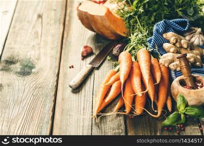 Healthy food cooking background. Vegetable ingredients. Fresh garden carrots, onions, pumpkins, ginger and spices on rustic wooden background