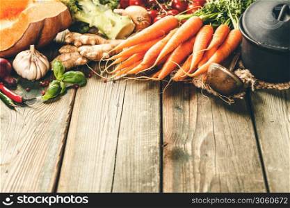 Healthy food cooking background. Vegetable ingredients. Fresh garden carrots, onions, pumpkins, ginger and spices on rustic wooden background. Healthy food cooking background. Vegetable ingredients, copy space
