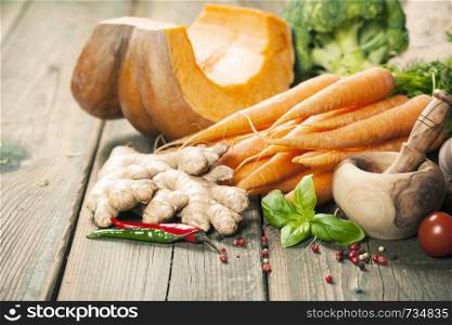 Healthy food cooking background. Vegetable ingredients. Fresh garden carrots, onions, pumpkins, ginger and spices on rustic wooden background. Healthy food cooking background. Warm and comfy autumn concept.