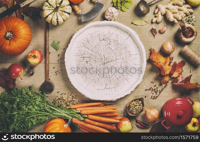 Healthy food cooking background. Vegetable ingredients. Fresh garden carrots, pumpkins, onions, apples and spices on rustic background with wooden tray in center, top view, copy space. Fresh garden carrots, pumpkins, onions, apples and spices on rustic background with wooden tray in center, top view, copy space