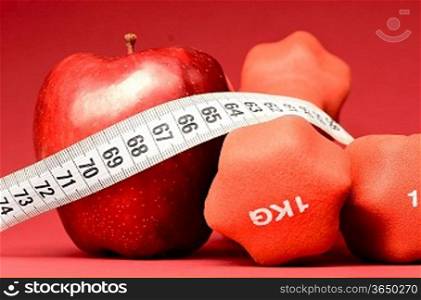 healthy food. Delicious apple with measuring tape and dumbbells on red