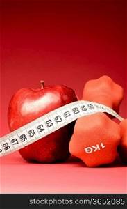 healthy food. Delicious apple with measuring tape and dumbbells on red