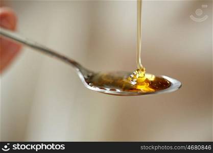 healthy food, eating and ethnoscience concept - close up of honey pouring to teaspoon