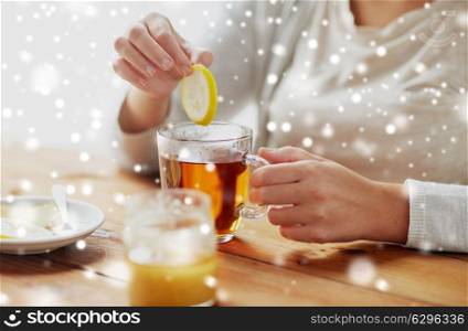 healthy food, eating and ethnoscience concept - close up of ill woman adding honey to tea cup with lemon and ginger over snow. close up of woman adding honey to tea with lemon