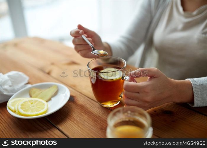 healthy food, eating and ethnoscience concept - close up of woman adding honey to tea cup with lemon and ginger