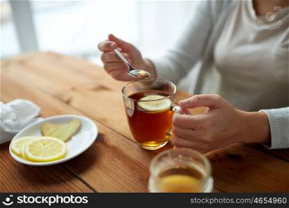 healthy food, eating and ethnoscience concept - close up of woman adding honey to tea cup with lemon and ginger