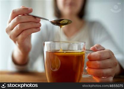 healthy food, eating and ethnoscience concept - close up of woman adding honey to tea cup with lemon