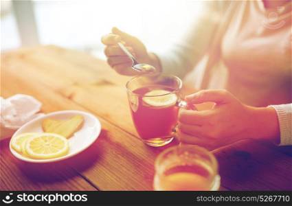 healthy food, eating and ethnoscience concept - close up of woman adding honey to tea cup with lemon and ginger. close up of woman adding honey to tea with lemon