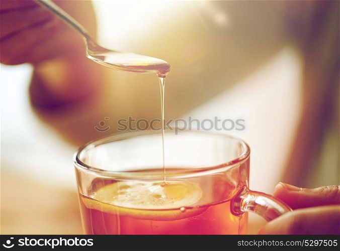 healthy food, eating and ethnoscience concept - close up of woman adding honey to tea cup with lemon. close up of woman adding honey to tea with lemon