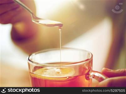 healthy food, eating and ethnoscience concept - close up of woman adding honey to tea cup with lemon. close up of woman adding honey to tea with lemon