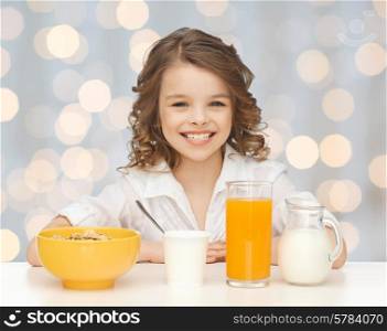 healthy food, eating, people and children concept - happy smiling beautiful girl having breakfast over holidays lights background