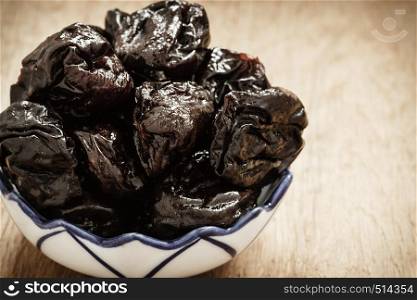 Healthy food, good cuisine. Closeup dried plums prunes fruits in bowl on wooden rustic table background