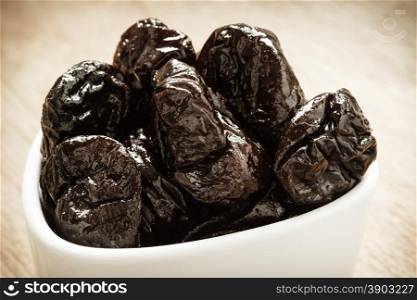 Healthy food, good cuisine. Closeup dried plums prunes fruits in white bowl on wooden rustic table background