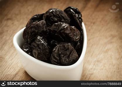 Healthy food, good cuisine. Closeup dried plums prunes fruits in white bowl on wooden rustic table background