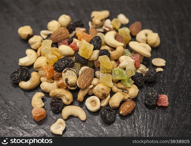 Healthy food; hazelnuts, almonds, cashew, raisin and dried fruits on a stone black background