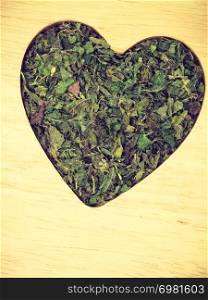 Healthy food, healing herbs, alternative herbal medicine concept. Dried herb nettle leaves in form of heart on wooden board with copy space. Dried nettle leaves heart shaped on wooden surface