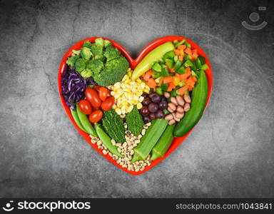 Healthy food selection clean eating for heart life cholesterol diet health concept. Fresh salad fruit and green vegetables mixed various beans nuts grain on red heart plate for healthy food vegan cook