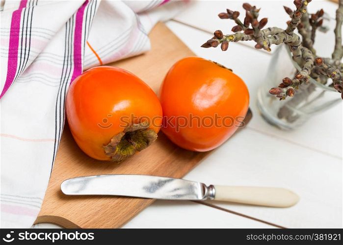 healthy food. Two persimmons are on the board, a knife and a towel