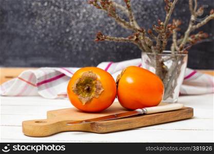healthy food. Two persimmons are on the board, a knife and a towel