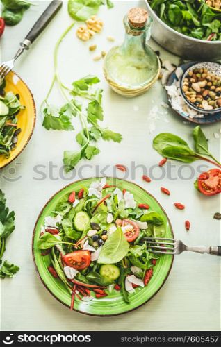 Healthy fresh green salad plate topped with various seeds and berries on light table background with olives oil and ingredients. Top view
