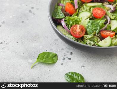 Healthy fresh vegetables salad with cucumbers and tomatoes, red onion and spinach in grey bowl on dark background with pepper
