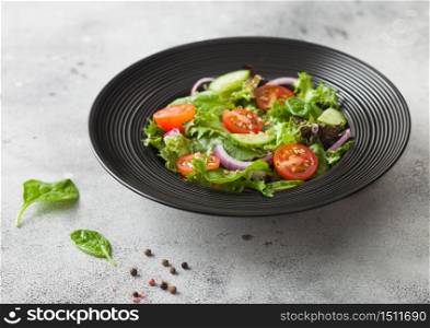 Healthy fresh vegetables salad with cucumbers and tomatoes, red onion and spinach in black bowl on dark background with pepper