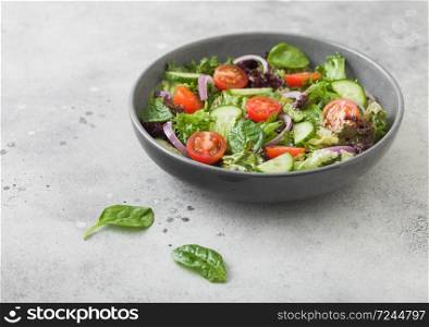 Healthy fresh vegetables salad with cucumbers and tomatoes, red onion and spinach in grey bowl on dark background with pepper