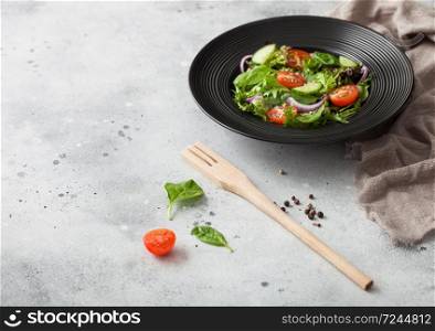 Healthy fresh vegetables salad with lettuce and tomatoes, red onion and spinach in black bowl on dark table background with spatula fork and kitchen towel.
