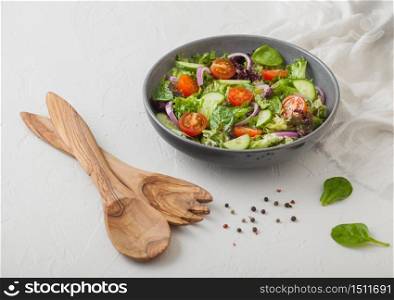 Healthy fresh vegetarian vegetables salad with lettuce and tomatoes, red onion and spinach in grey bowl plate on white table background with spatula fork and and spoon.