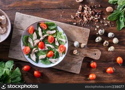Healthy freshly prepared salad of quail eggs, meat, tomatoes and spinach in a plate on a wooden board on the kitchen table. Dietary lunch. Flat lay. A plate of salad from boiled meat, quail eggs, spinach and tomatoes on a wooden board on the kitchen table. Dietary snack Flat lay