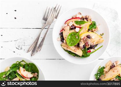 Healthy fruit and berry salad with fresh apples, cranberries, walnuts, italian ricotta cheese and spinach leaves. Delicious and nutritious diet dish for breakfast. Salad bowls on white wooden background. Overhead view