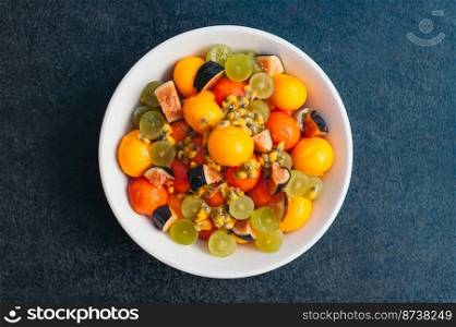 Healthy fruit platter. Selective focus. Bowl of cut colorful mango, figs, grape and papaya on dark background. Delicious vegetarian dish.