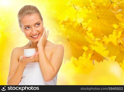 Healthy girl with body cream jar on autumnal background