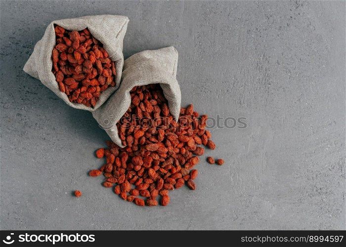 Healthy goji berries spilled out of small sack, isolated over grey background. Agriculture and nutrition concept. Superfood