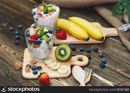 Healthy Greek yogurt with Granola and mixed berries on wooden table and many fruits. Food and dessert concept.