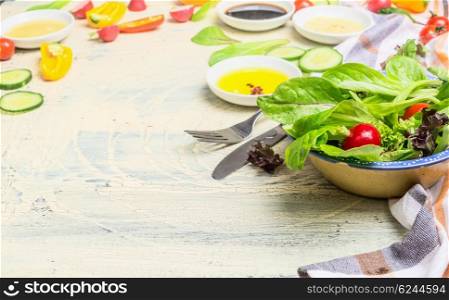 Healthy green salad dish with young lettuce leaves and various dressing ingredients on light wooden background. Healthy lifestyle or detox diet food concept