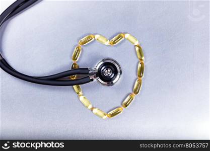 Healthy heart concept with fish oil capsules and stethoscope on stainless steel.