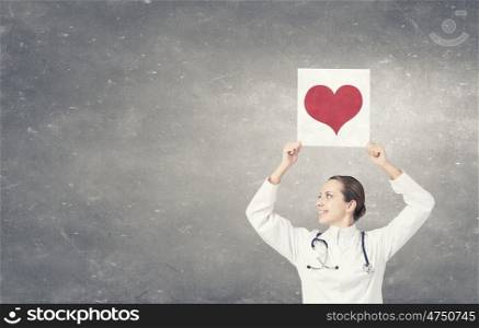 Healthy heart. Young female doctor holding paper sheet with red heart in hands