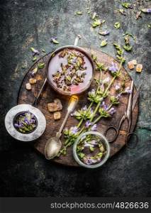 Healthy herbal tea preparation with fresh healing herbs, cup and vintage tea strainer on dark rustic wooden background, top view