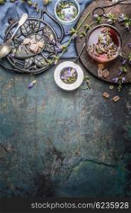 Healthy herbal tea with herbs leaves and flowers on dark rustic background. Tea with vintage tools and cup of tea, top view, place for text, border. Healthy drinks, detox or clean food concept