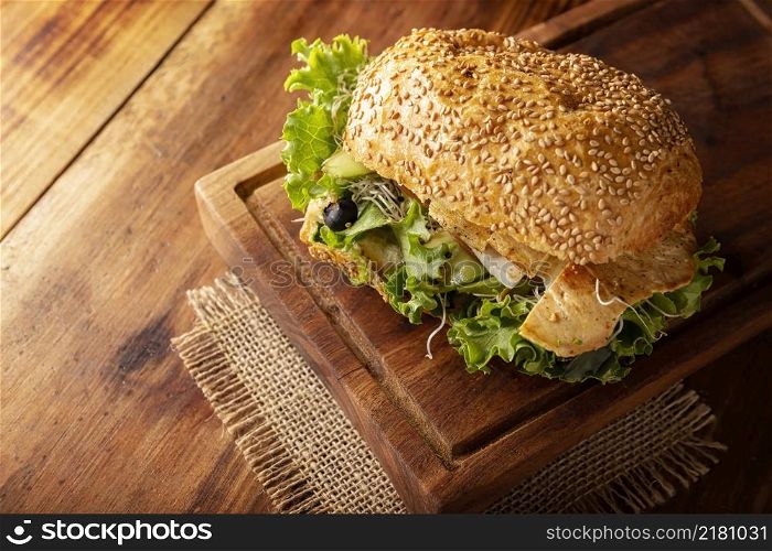 Healthy homemade sandwich with grilled chiken breast, lettuce, avocado, alfalfa germ and various other vegetables on rustic wooden board