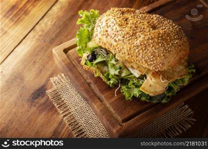 Healthy homemade sandwich with grilled chiken breast, lettuce, avocado, alfalfa germ and various other vegetables on rustic wooden board