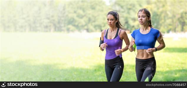 Healthy lifestyle banner - two beautiful fitness girls are jogging in the park on a sunny morning (copy space)